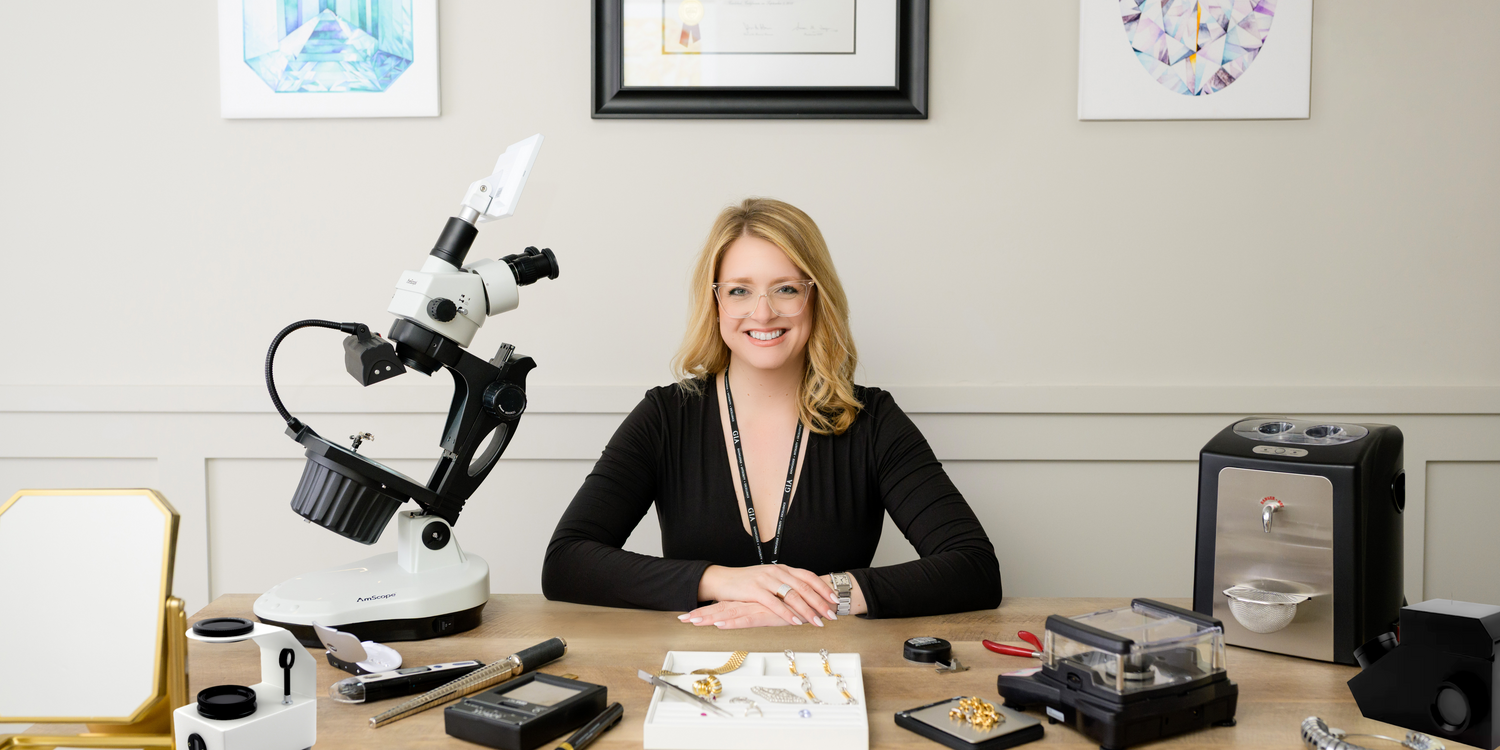 Smiling jeweler at a workbench with professional tools, a microscope, and fine jewelry pieces, showcasing expert craftsmanship at Devine Jeweler.