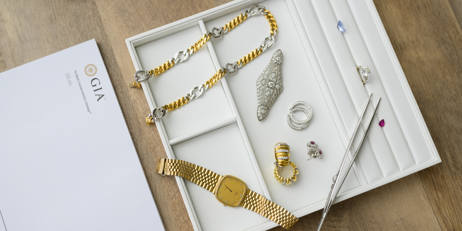 Luxury jewelry collection featuring gold and silver chains, diamond rings, vintage brooches, a gold watch, and loose gemstones with precision tools. Shop fine jewelry at Devine Jeweler.