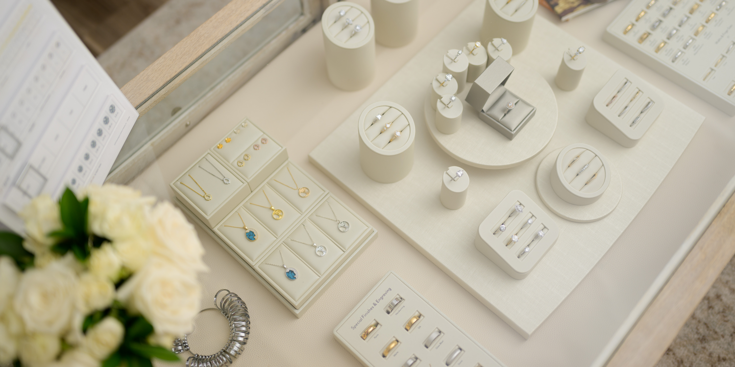 Elegant jewelry display featuring diamond rings, gold and silver necklaces with colorful gemstones, and wedding bands in a luxury showroom. Shop high-quality fine jewelry at Devine Jeweler.