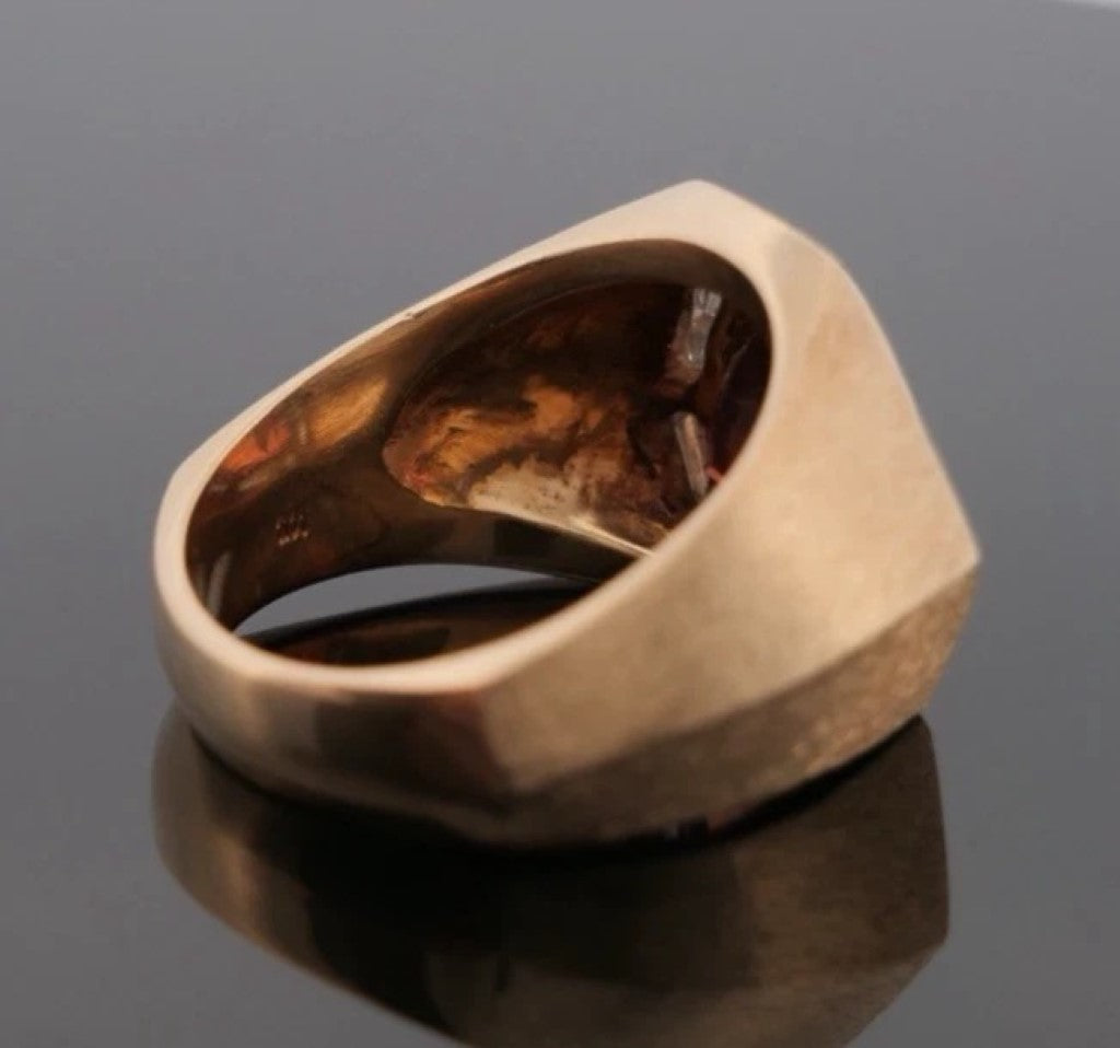 Gold ring with embedded amber on a reflective surface