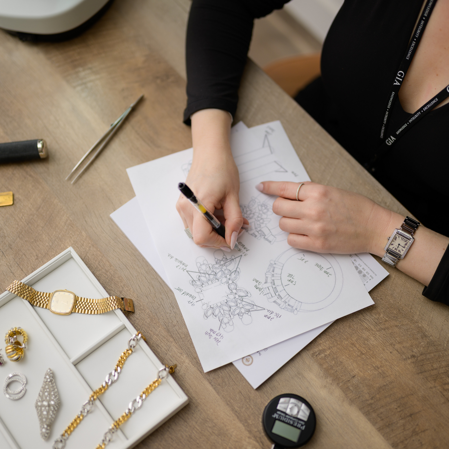 Jewelry designer sketching an intricate custom piece, surrounded by luxury watches and fine jewelry. Discover bespoke jewelry at Devine Jeweler.